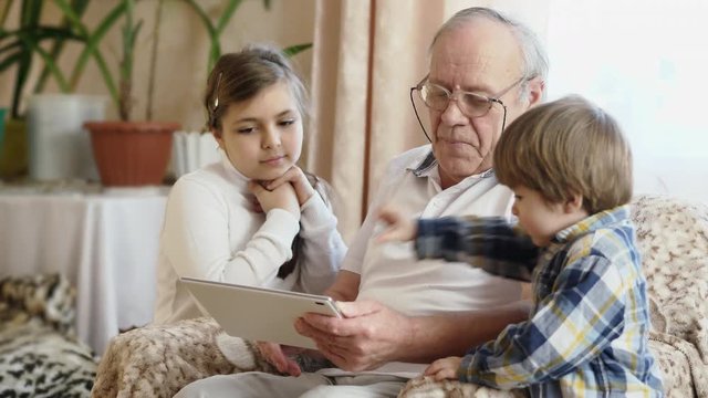 Grandfather using digital tablet with grandchildren