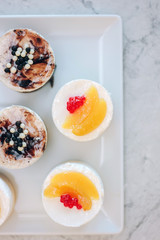 Flat view of beautiful cream cakes with berries and fruits on white ceramic plate.