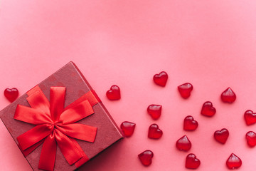 Red beautiful box with ribbon and bow on red background. Nearby are symbols in the form of a heart.