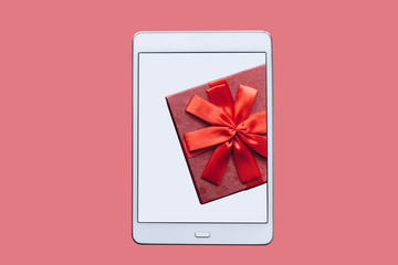 The concept of celebrating the event. A gift on the tablet screen that lies on a pink background.