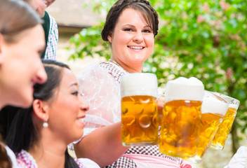 Kellnerin serviert Bier in Maßkrügen in Biergarten an drei Frauen und Mann