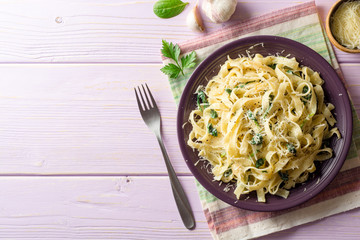 Tagliatelle pasta with spinach, garlic and Parmesan cheese on purple wooden background.