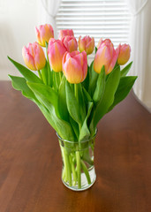 Pink tulips in a glass vase on dark wood table