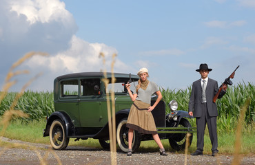 Two models get dressed up in 1930's style vintage fashion clothes and act the role of the gangster duo Bonnie and Clyde. - obrazy, fototapety, plakaty