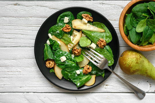vitamin salad with spinach leaves, pear, nuts and feta cheese in black plate