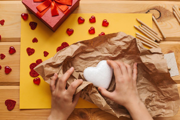 The girl holds a symbol in the form of a heart and wraps it in a craft paper and is going to send it to someone. Nearby lie various objects symbolizing the event.