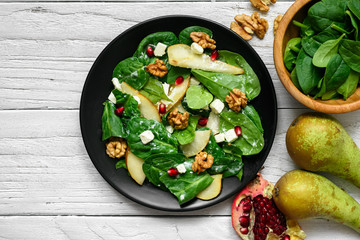 fresh spring salad with spinach leaves, pear, nuts, pomegranate and feta cheese in black plate