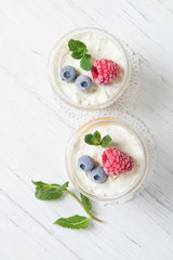 Two portions of homemade dessert cream with peaches, fresh berries and mint in a glass on a wooden table, top view