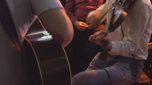 two young men perform in a small bar. one guy is playing the guitar, the other is playing the violin. live music in institutions. a warm image on the background of the bar. 4k