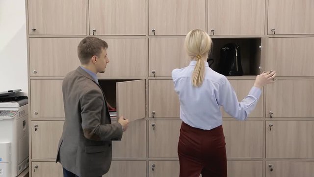 Man and woman open boxes and pick up things in modern office. Young managers taking personal belongings from cases and walking forward in company. Handsome guy and blonde in red skirt speak positively