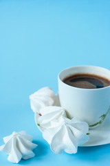 White cup of coffee with foam on a blue background with white meringues. Breakfast, dessert. Close up. Place for text. 