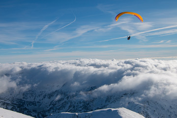 Paragliding above mountain peaks and clouds during winter sunny snowy day