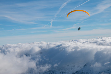Paragliding above mountain peaks and clouds during winter sunny snowy day