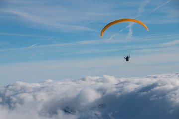 Paragliding above mountain peaks and clouds during winter sunny snowy day