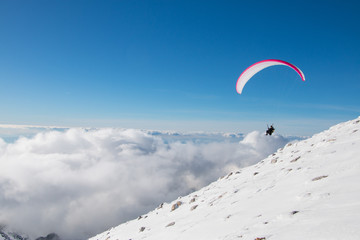 Paragliding above mountain peaks and clouds during winter sunny snowy day