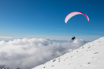 Paragliding above mountain peaks and clouds during winter sunny snowy day