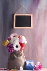 Flower bouquet with gifts and blackboard - Bouquet of roses, gerbera, tulips, and carnations, in a jute sack, surrounded by flowers and a gift box and a blank chalkboard in the background.