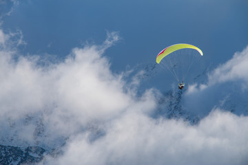 Paragliding above mountain peaks and clouds during winter sunny snowy day
