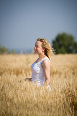 Portrait of young blond woman relaxing while walking on golden wheat field on a summer sunny day. Girl running on rye meadow. Outdoors. Countryside.