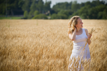 Fototapeta na wymiar Portrait of young blond smiling woman relaxing while walking on golden wheat field on a summer sunny day. Girl running on rye meadow. Outdoors. Countryside.