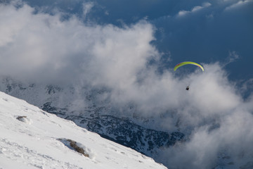 Fototapeta na wymiar Paragliding above mountain peaks and clouds during winter sunny snowy day