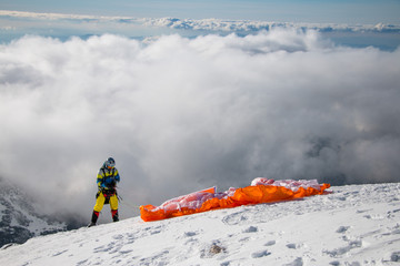 Paraglider starting to Paragliding above mountain peaks and clouds during winter sunny snowy day