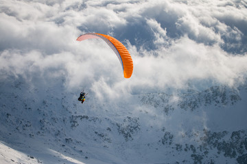 Paragliding above mountain peaks and clouds during winter sunny snowy day