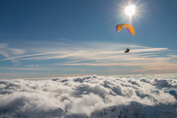 Fototapeta na wymiar Paragliding above mountain peaks and clouds during winter sunny snowy day