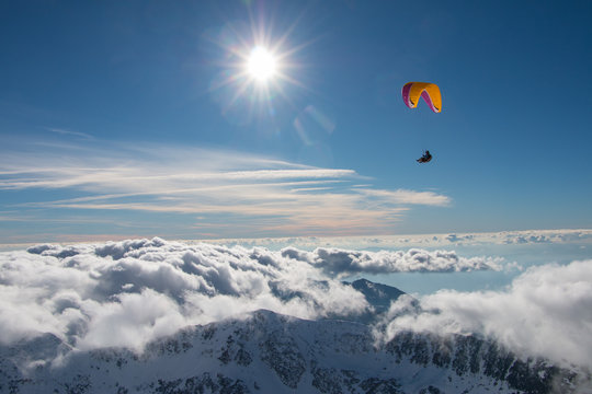 Paragliding above mountain peaks and clouds during winter sunny snowy day