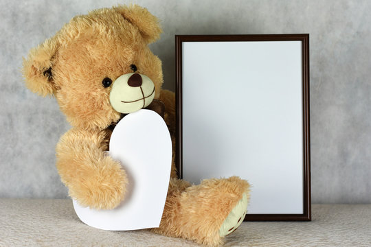 A loving teddy bear keeps a frame with a heart on the day of Saint Valentine's Day