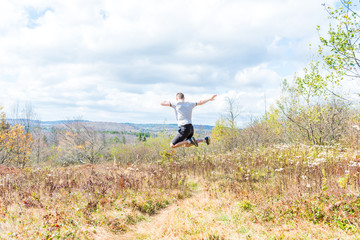 Fototapeta premium Young athletic, fit, free happy man running jogging jumping in autumn, fall, summer meadow field path hike in mid-air, muscles