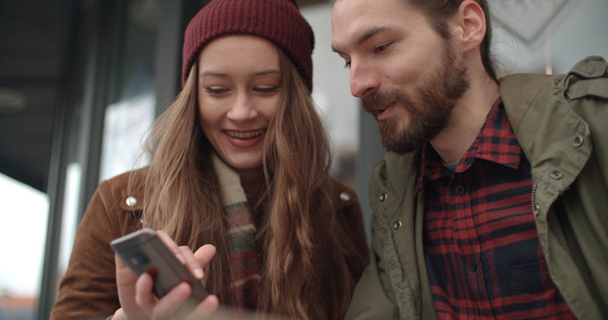 Beautiful couple looking at smartphone while sitting in outdoors restaurant.