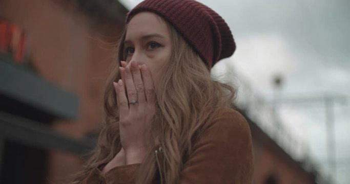 Beautiful worried woman sees somethnig and covers her mouth by hands in a city street.