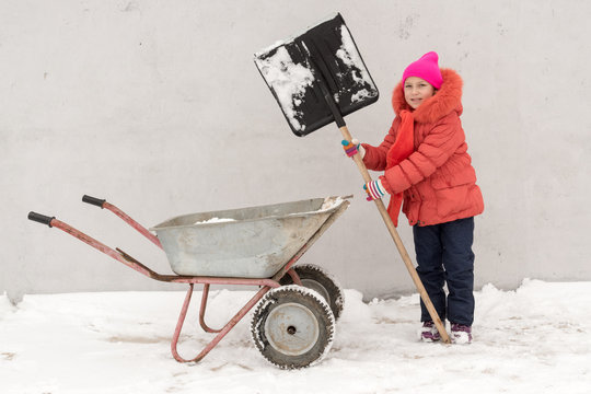 Cute little kid girl in colorful winter clothes playing in rural yard, outdoors during snowfall. Active outdoors leisure with children in winter. Happy boys with sister having fun with snow shovel