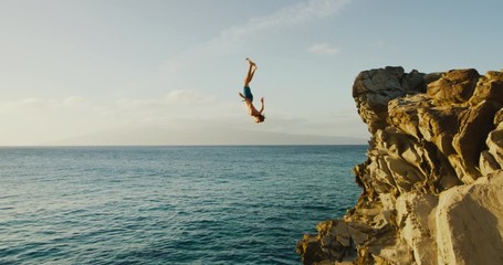Young man doing backflip cliff jumping into ocean at sunset
