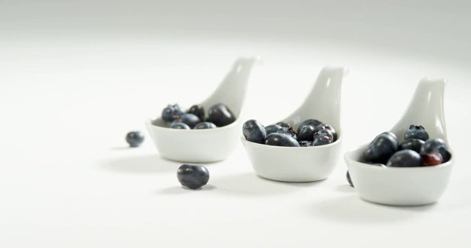 Blueberries in soup spoon placed on white surface  
