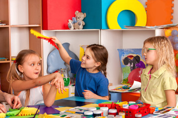 Fototapeta premium School children with scissors in kids hands cutting paper with teacher in class room. Children's project in kindergarten zone. Large group girls and boys together. Team of students makes paper fans.