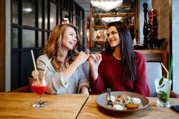 communication and friendship concept - smiling young women with nonalcoholic cocktails at cafe. two girlfriends blonde and brunette talk, joke and laugh