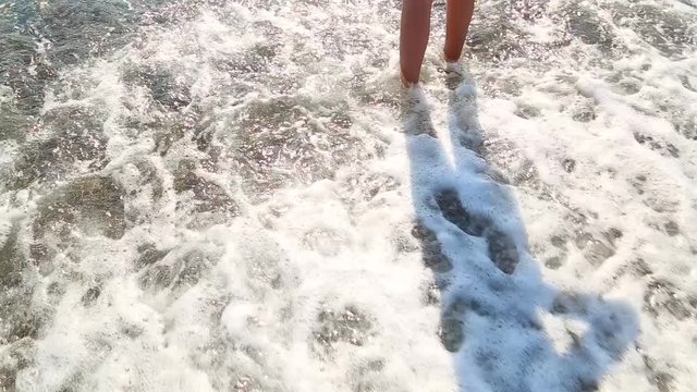 Barefoot cute little kid enters sunny sea water carefully.