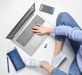 A modern young girl sits on a white floor and use a laptop. Generation z. The concept of...