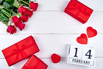 Red gift boxes with ribbon bow, two hearts, bouquet of red roses and wooden block calendar february 14 on white background. Greeting card mockup for Valentines Day. Love concept. Top view, flat lay