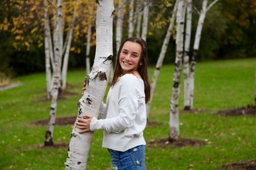 Portrait of a young teenage girl smiling in front of birch trees outdoors