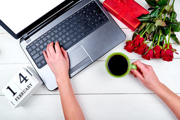 Top view of woman hand holding cup of coffee and working on open laptop computer, copy space. Valentines day background, free space. February 14 calendar. Flat lay