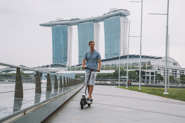 Young man riding an electric scooter in Singapore with an amazing view on the city. 