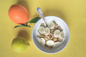 Top view of a bowl of cereals with yogurt and fruits, orange end lemon on bright yellow background. Fitness, healthy diet or breakfast concept 
