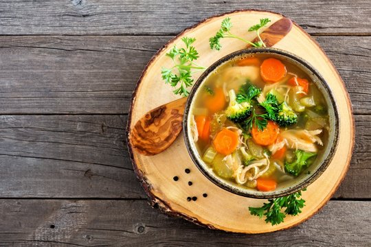 Homemade chicken vegetable soup, in a clay bowl with wooden server. Above view on a rustic wood background.