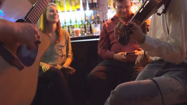 young people celebrate the day of St. Patrick. two men play the guitar and violin. live music in the bar. people are sitting on high taksoyah against the back of the bar. Holiday of drink and beer. 4