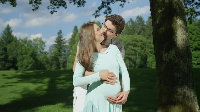 Portrait glowing expecting couple kissing in each other's embrace on sunny day