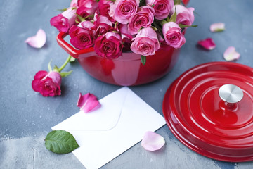 A bouquet of fresh pink roses, in a pan of red cast iron, on a gray stone background. Near the window. White envelope. Free place to write text or postcard.