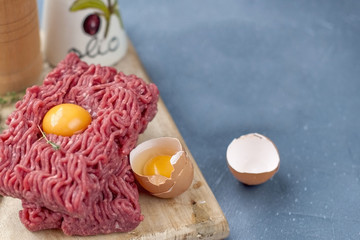 Fresh beef meat in minced meat, on a wooden board.Saw eggs. On a gray stone background. Free space for writing text.